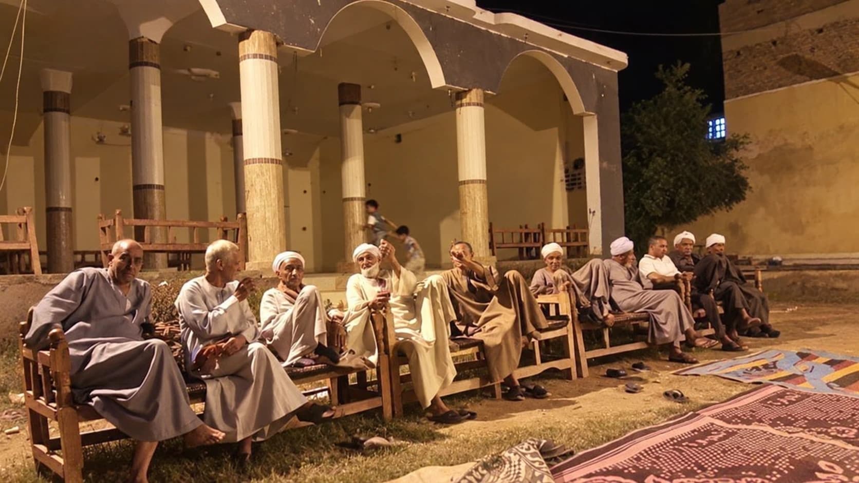 مجلس رجال أمام ديوان آل يونس مع ظهور صغار في الخلف، من الصور المرفقة بالمادة العائلية